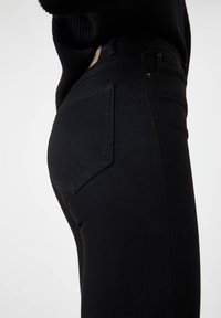 Jeans de mezclilla negra con diseño ajustado, que cuentan con un bolsillo trasero, costuras visibles y una tela texturizada.