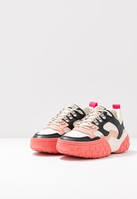 Klobige Sneakers mit einer Mischung aus beigen, rosa und schwarzen Materialien, Gummisohlen mit kreisförmigen Mustern und einer auffälligen rosa Fersenschlaufe.