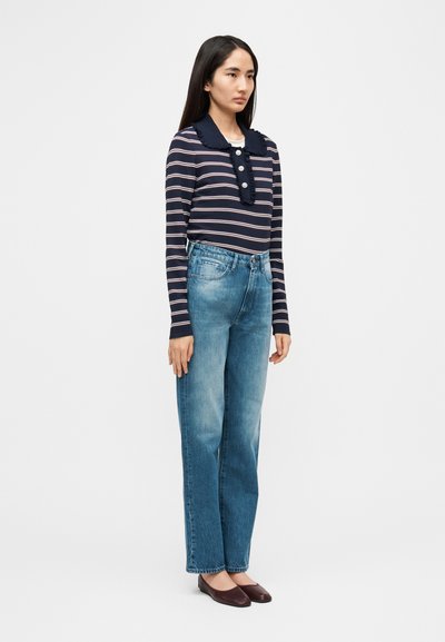 Ναυτικό ριγέ τοπ με μακριά μανίκια, τσαλακωμένο γιακά και λεπτομέρειες κουμπιών, σε συνδυασμό με τζιν ευθείας γραμμής ανοιχτού χρώματος και σκούρα καφέ φλατ παπούτσια.