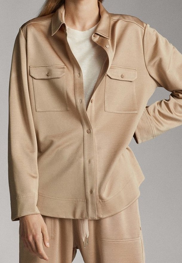 Chemise beige à boutons en tissu doux, dotée de deux poches avant et d'une coupe décontractée. Assortie à une couche intérieure de couleur claire.