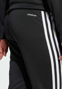 Czarne spodenki sportowe z białymi paskami po bokach, wykonane z gładkiego materiału, z logo "AEROREADY" z tyłu.