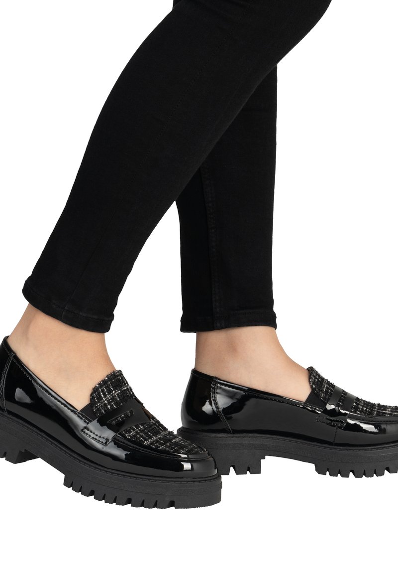 Mocasines de charol negro con un acento de tela texturizada en la parte superior y una suela de goma gruesa con relieve. Combinados con jeans negros.