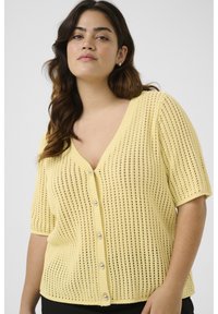 Cardigan en tricot jaune à manches courtes avec un col en V, doté d'une fermeture à boutons et d'un motif de points ouverts, offrant un aspect texturé et respirant.
