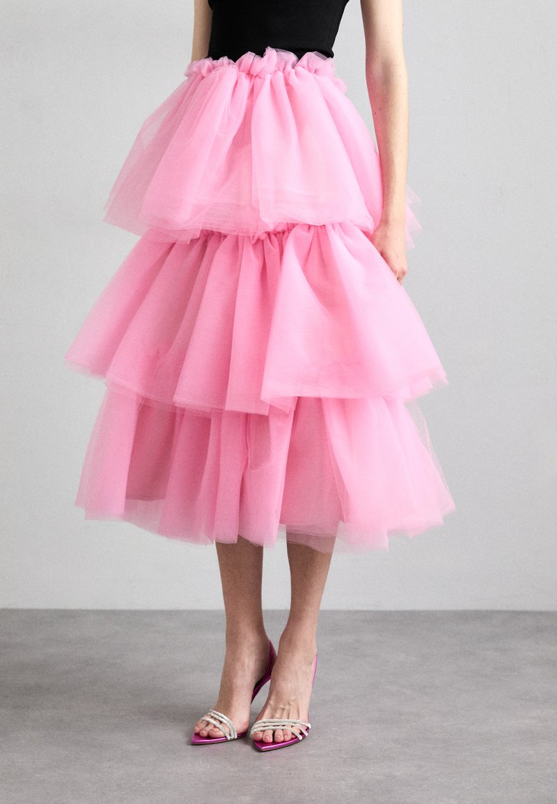 Roze tule rok met drie gelaagde volants, en een geraffineerde tailleband met een doorschijnende textuur; gecombineerd met roze hakken met decoratieve banden.
