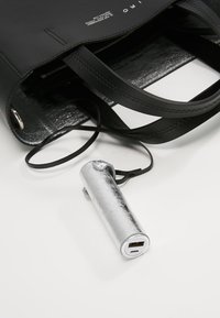 Black leather tote bag with two handles, featuring a shiny silver portable charger with a USB port visible outside the bag.