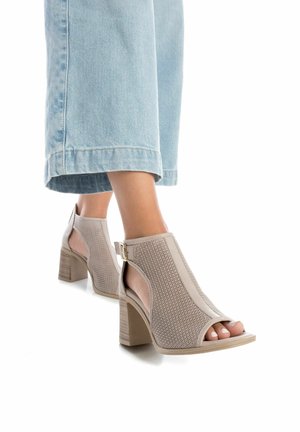 Sandalias de tacón abiertas en la punta de color beige, con parte superior de malla texturizada, paneles laterales sólidos, una correa con hebilla y un tacón en bloque con patrón de madera.