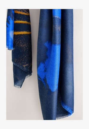 Dva visiace šály s abstraktnými vzormi v odtieňoch modrej a tmavomodrej, jeden so žltými horizontálnymi pruhmi a ošúchanými okrajmi.