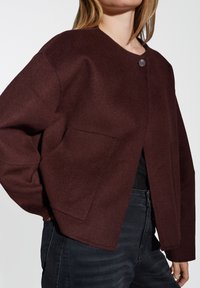 Burgundy wool-blend jacket with a round neckline, button closure, and two front pockets; features a relaxed fit and slightly oversized sleeves.