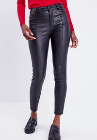 Pantalons en simili cuir noir à taille haute, coupe slim, poches zippées à l'avant et texture lisse. Associés à des chaussures noires à enfiler.