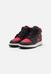 Black and red mid-top sneakers with smooth leather, perforated toe, white sole, and prominent Nike logo. Laces and accents are black.