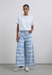 Oversized white t-shirt paired with wide-leg light blue denim jeans featuring a wavy white pattern. White sneakers complete the look.