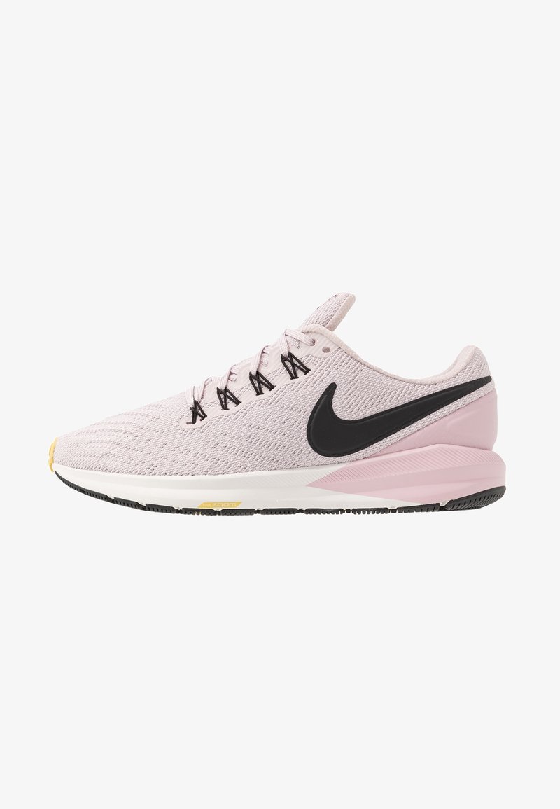 Chaussure de course rose pâle avec le logo Nike noir, lacets noirs, semelle intermédiaire blanche et accents noirs et jaunes sur la semelle extérieure, vue latérale.