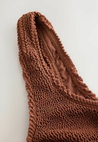Close-up of a brown textured fabric strap with a ruched, crinkled pattern and a smooth inner lining on a light background.