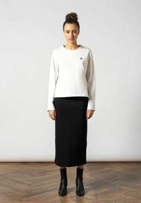 Langærmet hvid top med et lille logo, kombineret med en tætsiddende sort midi-nederdel. Modellen har sorte ankelstøvler på. Glat stof og afslappet pasform.