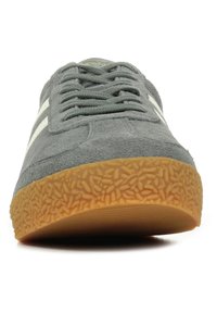 Sneaker grigia in suede con strisce bianche, suola in gomma piatta e testurizzata, punta rotonda e linguetta imbottita. I lacci si estendono sopra il collo imbottito.