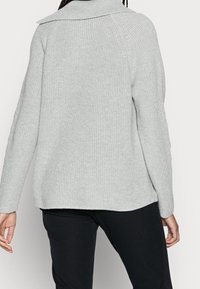 Maglione grigio lavorato a maglia con colletto alto e texture a coste; presenta maniche lunghe e una vestibilità rilassata, che arriva fino ai fianchi.