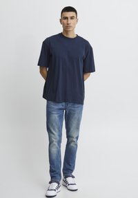 Navy blue cotton t-shirt with a round neck, short sleeves, paired with light blue distressed jeans and white sneakers with navy accents.