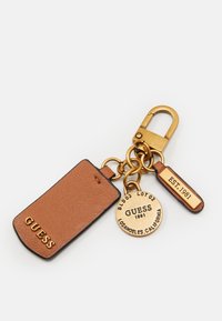 Portachiavi con un'etichetta in pelle marrone e un pendente circolare dorato, caratterizzato da incisioni "GUESS 1981" e "LOS ANGELES, CALIFORNIA".