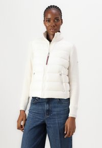 Hvid pudejakke med ribbede lange ærmer, lynlåse foran og en subtil stribet accent. Båret med blå denim jeans.