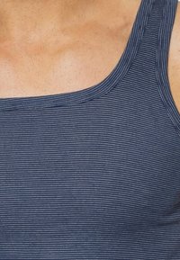 Granatowy top na ramiączkach z poziomymi białymi paskami, z szerokim dekoltem i wąskimi ramiączkami. Gładka faktura, bawełniany lub podobny materiał.