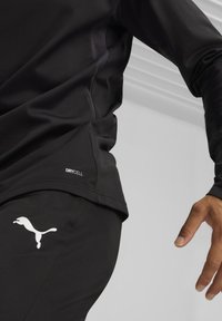 Schwarzes Sportoberteil mit glatter Textur und enganliegendem Design, mit "DRYCELL"-Branding und Logo auf der Hose. Leichtes, feuchtigkeitsableitendes Material.