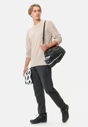 Schwarze Umhängetasche, beiges Langarmshirt, schwarz tapering Hosen, schwarze Fahrradschuhe und ein weißer Fahrradhelm.