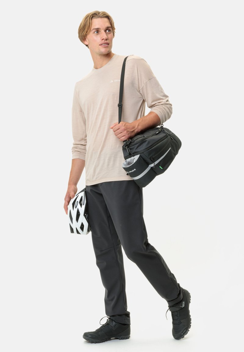 Borsa a spalla nera, camicia a maniche lunghe beige, pantaloni neri a gamba affusolata, scarpe da ciclismo nere e un casco da ciclismo bianco.