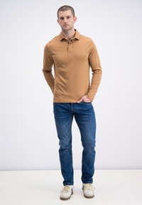 Koszulka polo z długim rękawem w kolorze piaskowym z kołnierzykiem, zestawiona z niebieskimi dżinsami. Białe trampki z szarymi akcentami. Prosty, dopasowany fason.