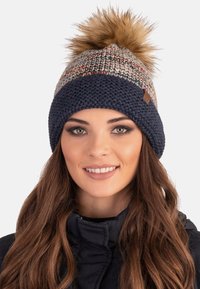 Berretto lavorato a maglia con un motivo multicolore sulla parte superiore, banda a coste blu scuro e un grande pompon sintetico color beige.