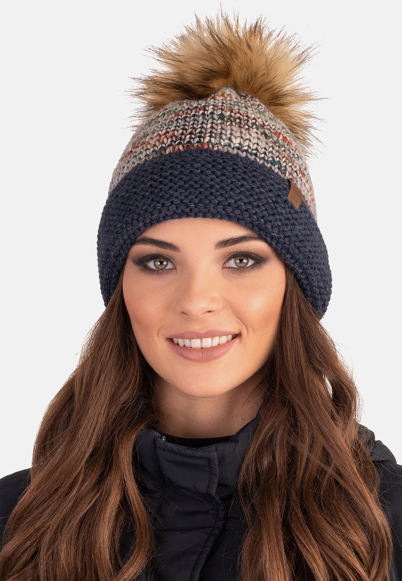 Berretto lavorato a maglia con un motivo multicolore sulla parte superiore, banda a coste blu scuro e un grande pompon sintetico color beige.