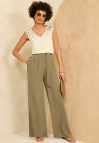 V-neck tank top with sequin details, paired with high-waisted, wide-leg olive green trousers, carrying a textured pouch bag.