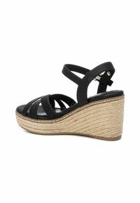 Sandalias de cuña de cuero negro con correas cruzadas, tacón envuelto en yute y detalles texturizados. Correa en el tobillo ajustable para un mejor ajuste.