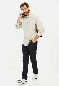 Beige overhemd met lange mouwen en knopen, marineblauwe cargobroek en witte sneakers met zwarte accenten. Gestructureerde stof en praktische zakken.