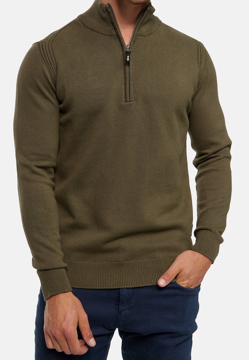 Pullover lavorato a maglia verde oliva con colletto a mezza zip. Presenta polsini e orlo a coste, tessuto testurizzato e un design aderente.