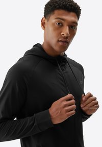 Sudadera con cremallera negra y un acabado suave y mate; cuenta con un corte relajado, capucha con cordones y un sutil logo en el pecho.