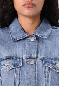 Helehall denimjakk klassikalise kraega, hõbedaste nööpidega ja kahe rinna taskuga. Omab täiustunud tekstuuri ja kahekordse õmblusega õmblusi.