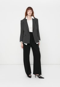 Blazer gris de doble botonadura y rayas finas, sobre una camisa blanca, combinado con pantalones negros de pierna ancha y zapatos de tacón negros con acentos de corte.