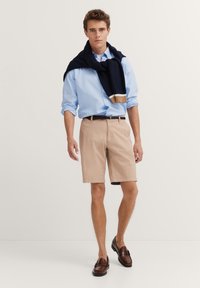 Hellblaues Button-up-Hemd, khakifarbene Shorts, marineblauer Pullover über die Schultern gelegt, braune Schuhe. Lässiges Sommeroutfit mit einfachen, klaren Linien.