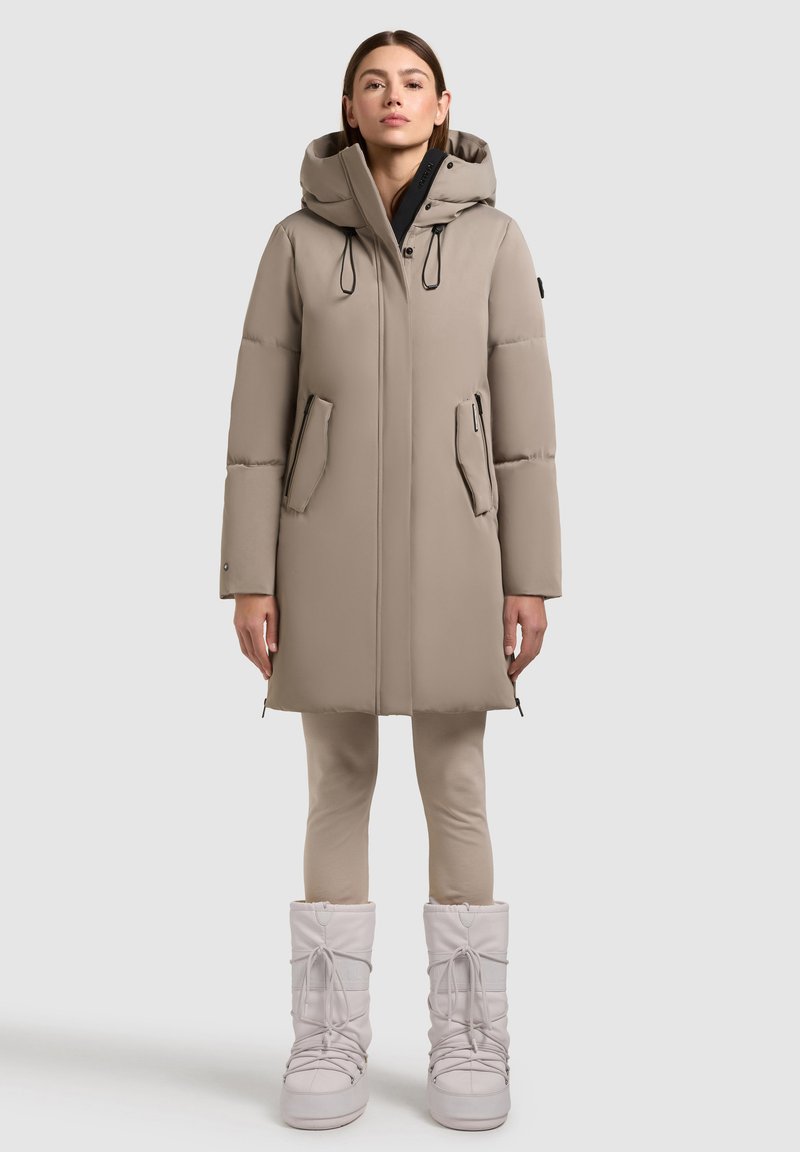 Beige puffer coat with adjustable hood, two front pockets, and elastic drawstrings. Paired with beige leggings and light-colored winter boots.