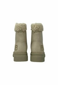 Un paio di stivaletti beige alla caviglia con polsini pelosi e lettera "B" in strass decorativa sul tallone, visti da dietro.