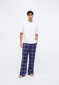 Fehér pamut póló "TOMMY HILFIGER" logóval, kék kockás flanel nadrággal, piros és krémszínű kockás mintázattal párosítva.