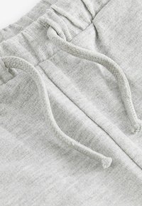 Pantalon de survêtement gris en tissu texturé, dotés d'une ceinture à cordon de serrage et de détails cousus le long des bords.