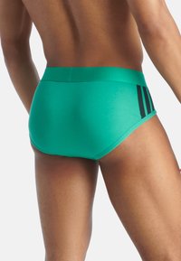 Boxer de bain verts au design ajusté, avec une couleur unie et des rayures noires sur le côté. Texture lisse et ceinture élastique.