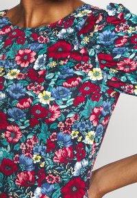 Robe fleurie avec des manches bouffantes mettant en avant un fond marine décoré de fleurs rouges, roses et bleues ainsi que de feuillage vert. Texture de tissu lisse.