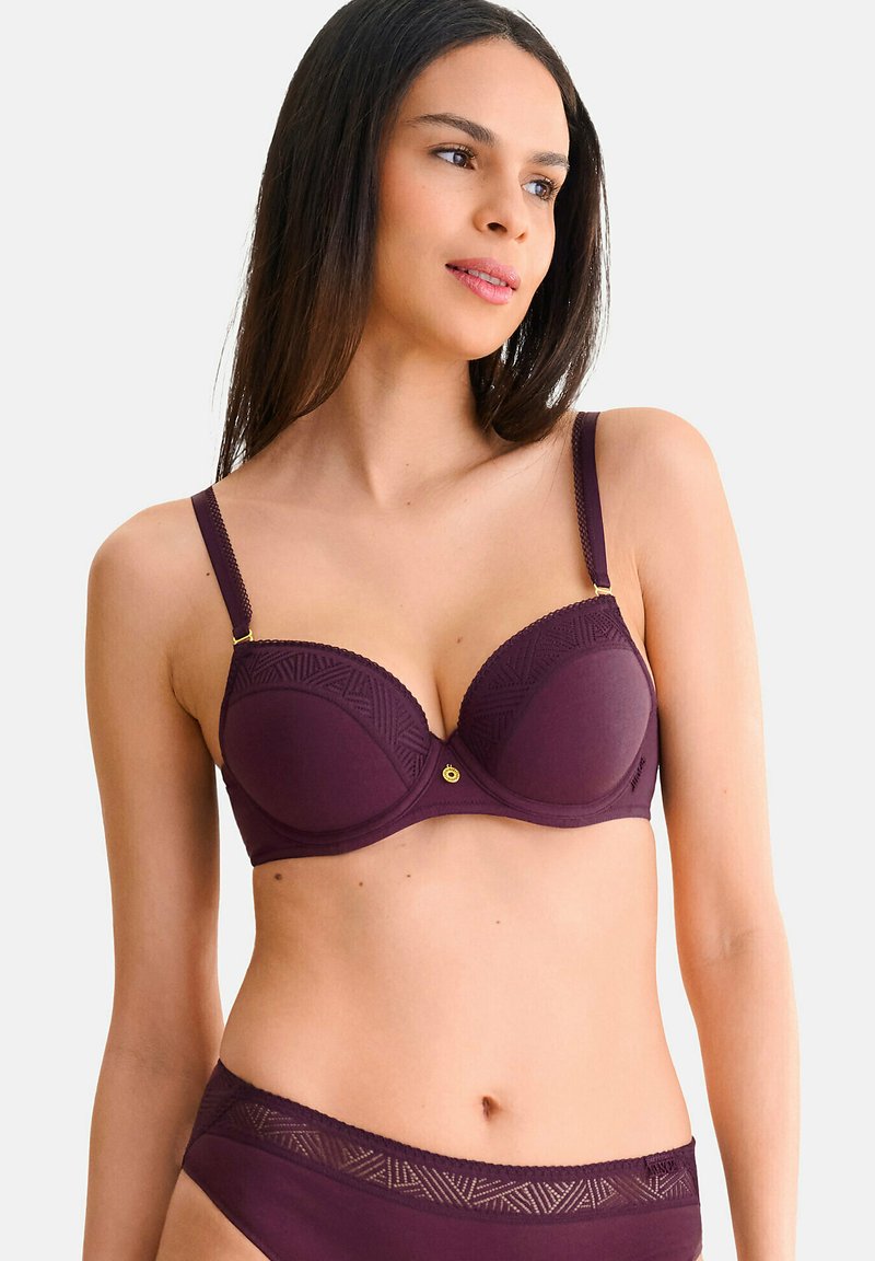 Bordeaux beha met gepadde cups, geometrische kantaccenten, verstelbare bandjes en een gouden detail in het midden. Glad stofoppervlak.