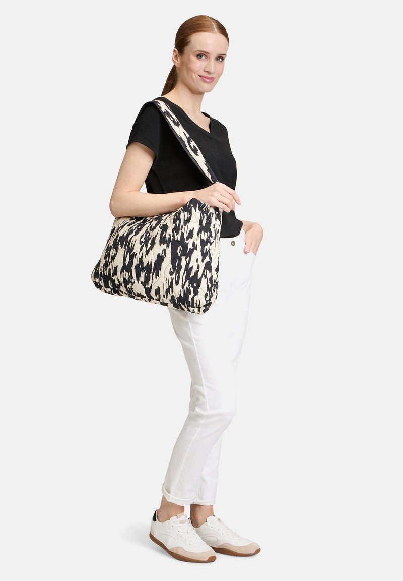 Grand sac à épaule en tissu avec un motif abstrait noir et crème. Texture douce, forme arrondie, longue bandoulière et fermeture éclair.