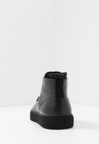 Černé kožené kotníkové boty s matným povrchem, se strukturovanou černou gumovou podrážkou a zadním poutkem pro snadné obouvání.