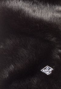 Tessuto in pelliccia sintetica nera con una consistenza morbida e liscia, con un logo "REPLAY" a forma di diamante argentato in bella vista.