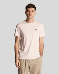 Ljusrosa t-shirt med kort ärm i mjukt bomull, med en liten gul fjäril som logotyp på vänster bröst. Enkel rundhalsad design.