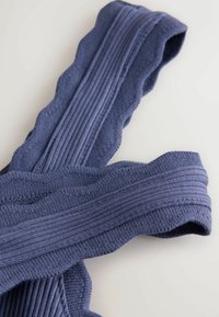 Gros plan d'un vêtement tricoté bleu plié avec des bords côtelés et festonnés sur une surface claire.